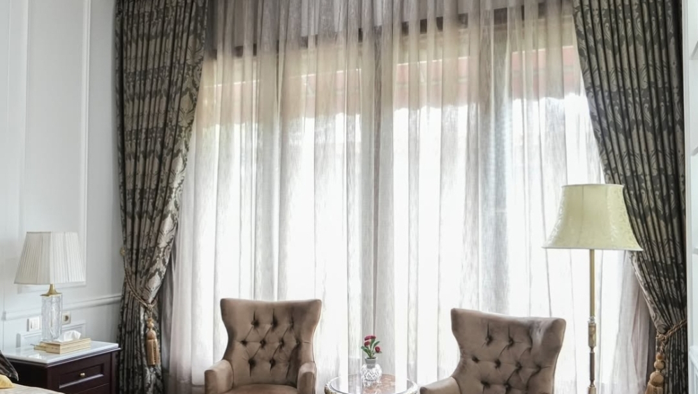 Grand bedroom with custom patterned drapes and sheers, showcasing expert curtain service for luxurious interiors.
