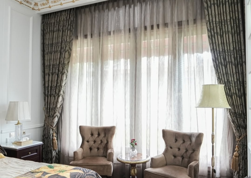 Grand bedroom with custom patterned drapes and sheers, showcasing expert curtain service for luxurious interiors.